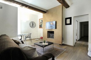 A modern living room with a sofa, coffee table, and fireplace. A TV is mounted on the wall, and there is a framed picture above the fireplace.