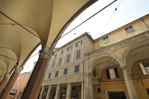 An interior with classical architecture, including arches and columns, and a building facade with windows and shutters.