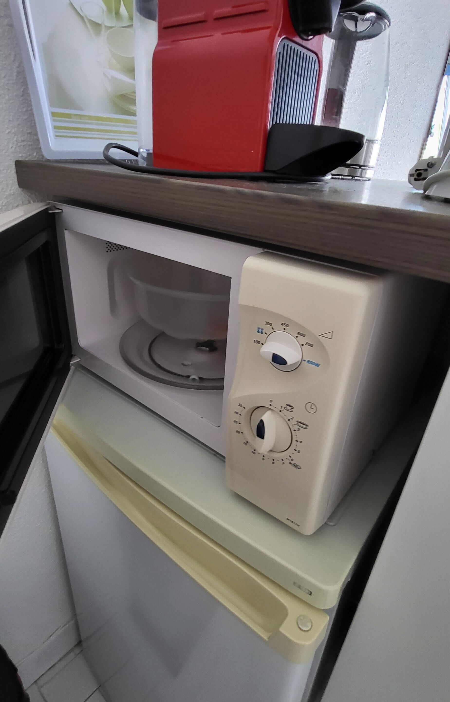 Una cocina compacta con microondas, un refrigerador pequeño y un electrodoméstico rojo encima del microondas.