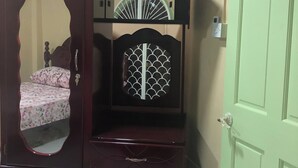 Quarto com um guarda-roupa de madeira grande, uma cama com roupa de cama floral e uma porta verde.