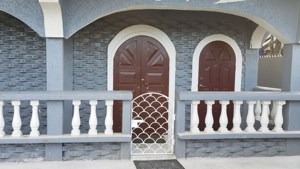 Fachada de edifício com três portais em arco, cada um com porta castanha e grade decorativa branca.
