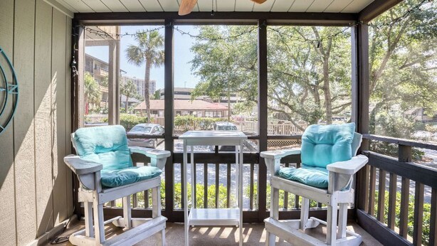 A balcony with two white chairs and a small table, overlooking a parking area and buildings. - Beach Condo. Across from Ocean Annie's. 1st floor beach condo with large pool. (Myrtle Beach)