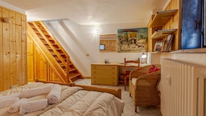 Een slaapkamer met een houten trap, een bed met opgerolde handdoeken, een bureau, een stoel en een radiator.
