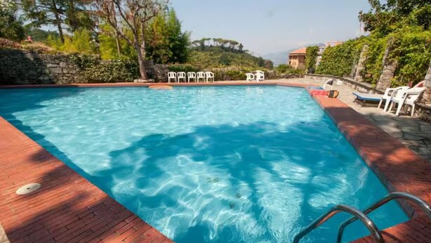 Ein rechteckiger Swimmingpool mit klarem, blauem Wasser, umgeben von einer Ziegelterrasse und weißen Liegestühlen.