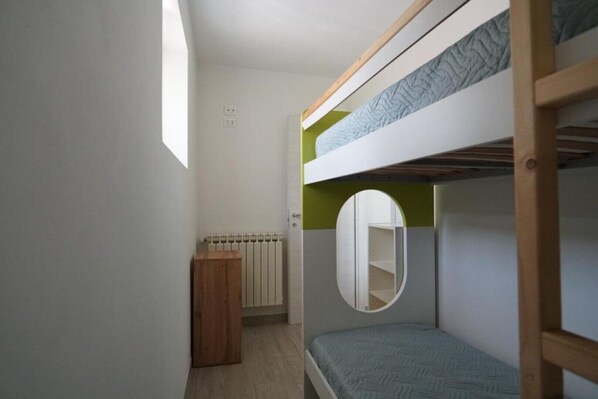 Une chambre avec un lit superposé, une fenêtre, un radiateur et une armoire en bois.