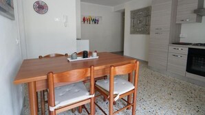 A dining area with a wooden table and chairs, a white wall with a clock and a phone, and a kitchen area with cabinets and a stove. - Da Rita - Two-bedroom apartment. (Crone)