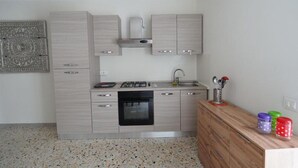 A compact kitchen with a gas stove, oven, and sink. There is a wooden cabinet and a decorative wall piece. - Da Rita - Two-bedroom apartment. (Crone)