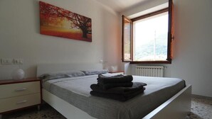 A bedroom with a bed, a nightstand, a painting, a window, and a radiator. - Da Rita - Two-bedroom apartment. (Crone)