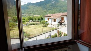 A window view of a rural area with a house, a road, and mountains in the background. - Da Rita - Two-bedroom apartment. (Crone)