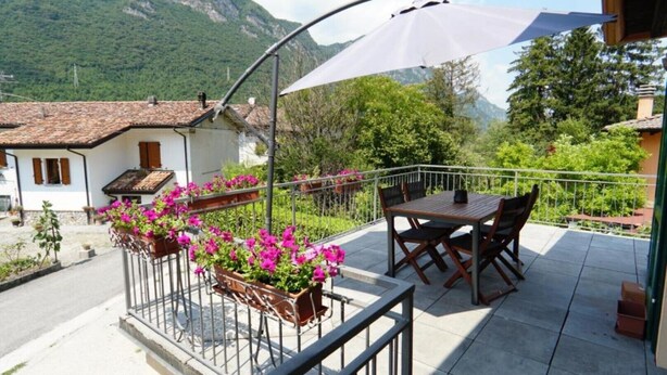 A balcony with a table and chairs, surrounded by potted plants with pink flowers. - Da Rita - Two-bedroom apartment. (Crone)