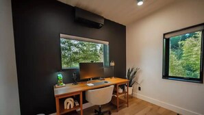 Un espace de bureau moderne avec un bureau en bois, un ordinateur et une chaise blanche. Il y a une fenêtre donnant sur des arbres et un mur noir.
