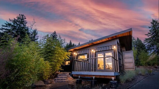 Une cabane moderne avec une façade en bois, de grandes fenêtres et un escalier menant à l’entrée.