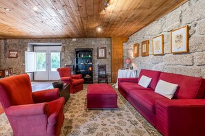 Uma sala de estar aconchegante com parede de pedra, teto de madeira, mobiliário vermelho e quadros emoldurados.