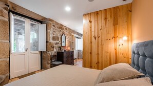 Ein Schlafzimmer mit Steinwand, Holzpaneelen, einem Bett mit Kissen, einem Schminktisch und einem Sessel.