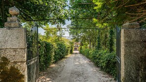 Ein schmaler, gepflasterter Weg, der von Steinmauern und schmiedeeisernen Toren gesäumt wird und zu einem Gebäude in der Ferne führt.