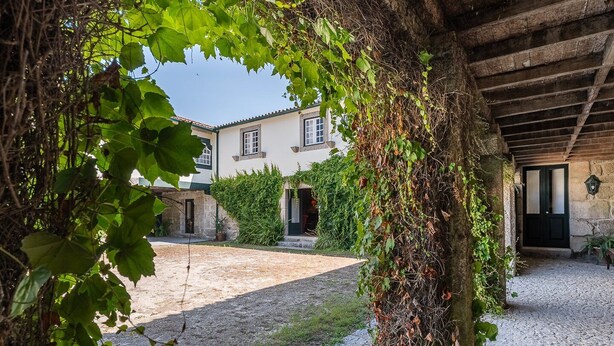 Ein Innenhof mit einem Steinweg, ein Gebäude mit Ziegeldach und ein überdachter Bereich mit Holzboden.