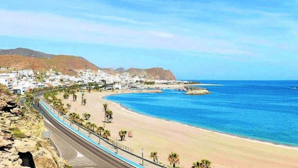 Eine Küstenstadt mit Strand, einer Straße mit blauer Absperrung und Gebäuden im Hintergrund.