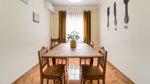 A dining room with a wooden table and chairs, a potted plant, and a window with curtains.