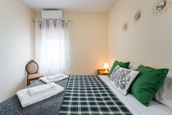 Una camera da letto con un letto, una sedia, un comodino, una lampada e una finestra con tende.