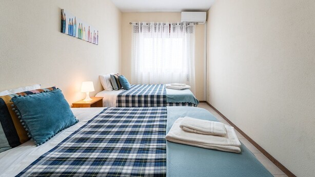 A hotel room with two beds, each with a blue and white checkered bedspread, a nightstand with a lamp, and a wall-mounted picture of colored pencils.