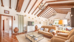 A spacious living room with a high ceiling, wooden beams, a television, a sofa set, and a dining area with a table and chairs. - Refreshing poolside escape in Ponte de Sor (Portalegre)