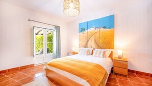 A bedroom with a bed, a nightstand, a lamp, a painting, and a view through a glass door. - Refreshing poolside escape in Ponte de Sor (Portalegre)