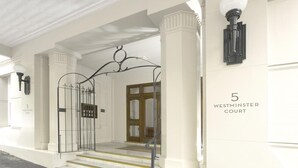 Eine imposante Eingangshalle mit einem schmiedeeisernen Tor, Stufen, die zu einer Holztür führen, und einem Schild mit der Aufschrift '5 Westminster Court'.