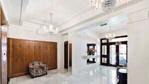 Eine großzügige Lobby mit Schachbrettmuster-Boden, einer Holzwand und einem Sessel mit Leopardenmuster, darüber ein Kronleuchter.