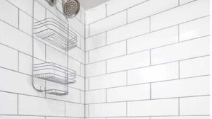 A corner shower with white tiled walls and a metal showerhead. - The Delightful Den (Philadelphia)