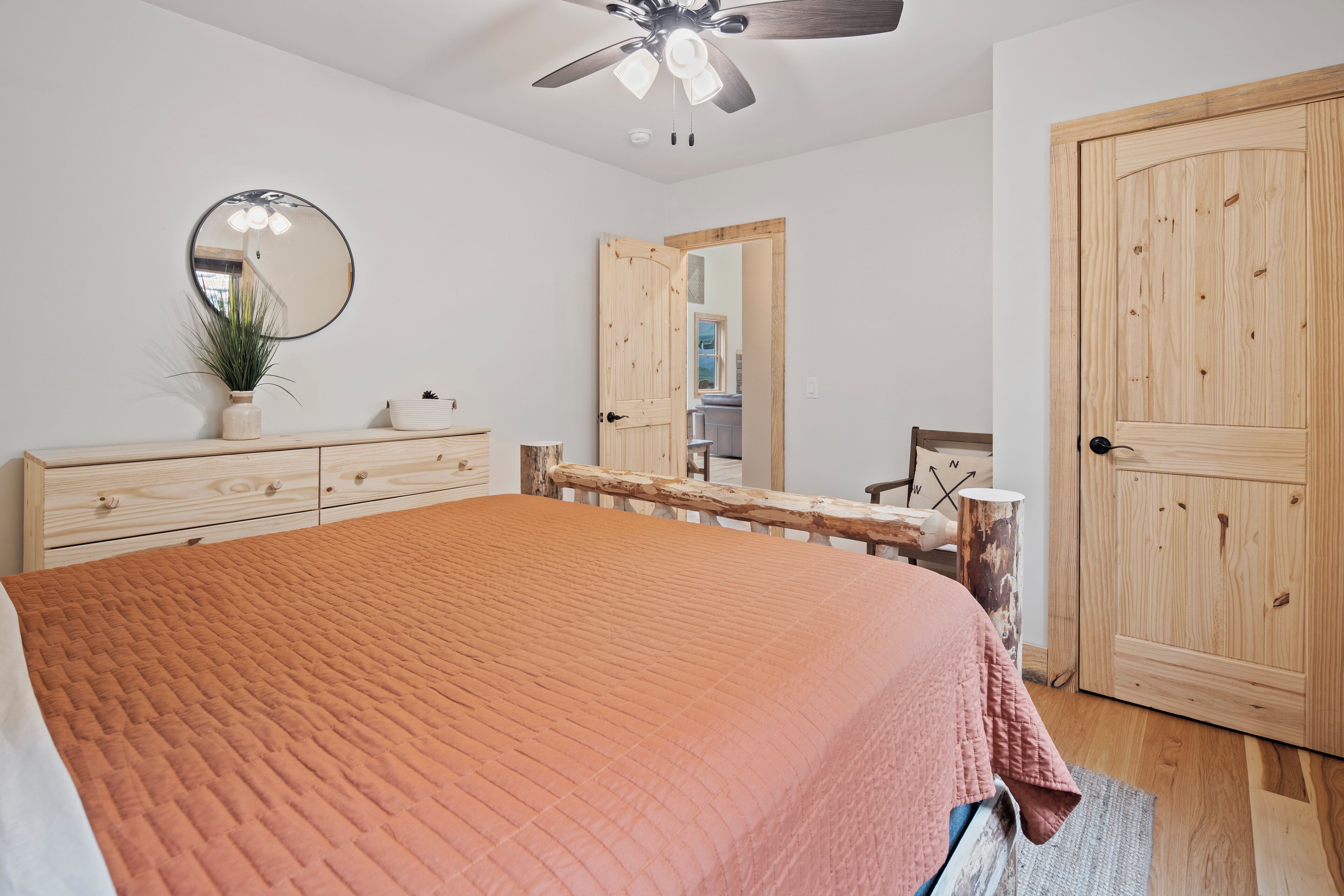 A bedroom with a large bed, a wooden wardrobe, a mirror, and a ceiling fan.