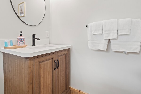 A bathroom with a wooden cabinet, a white sink, and a towel rack with three white towels.
