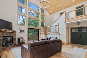 A spacious living room with a large brown leather sofa, a stone fireplace, and a wooden staircase leading to an upper level.