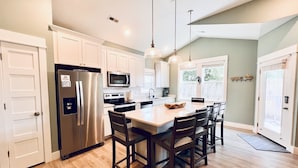 A modern kitchen with white cabinets, stainless steel appliances, and a central island with chairs. - *New* Oceanside,Pool,Walk 2 the beach,No Stairs (Corolla)
