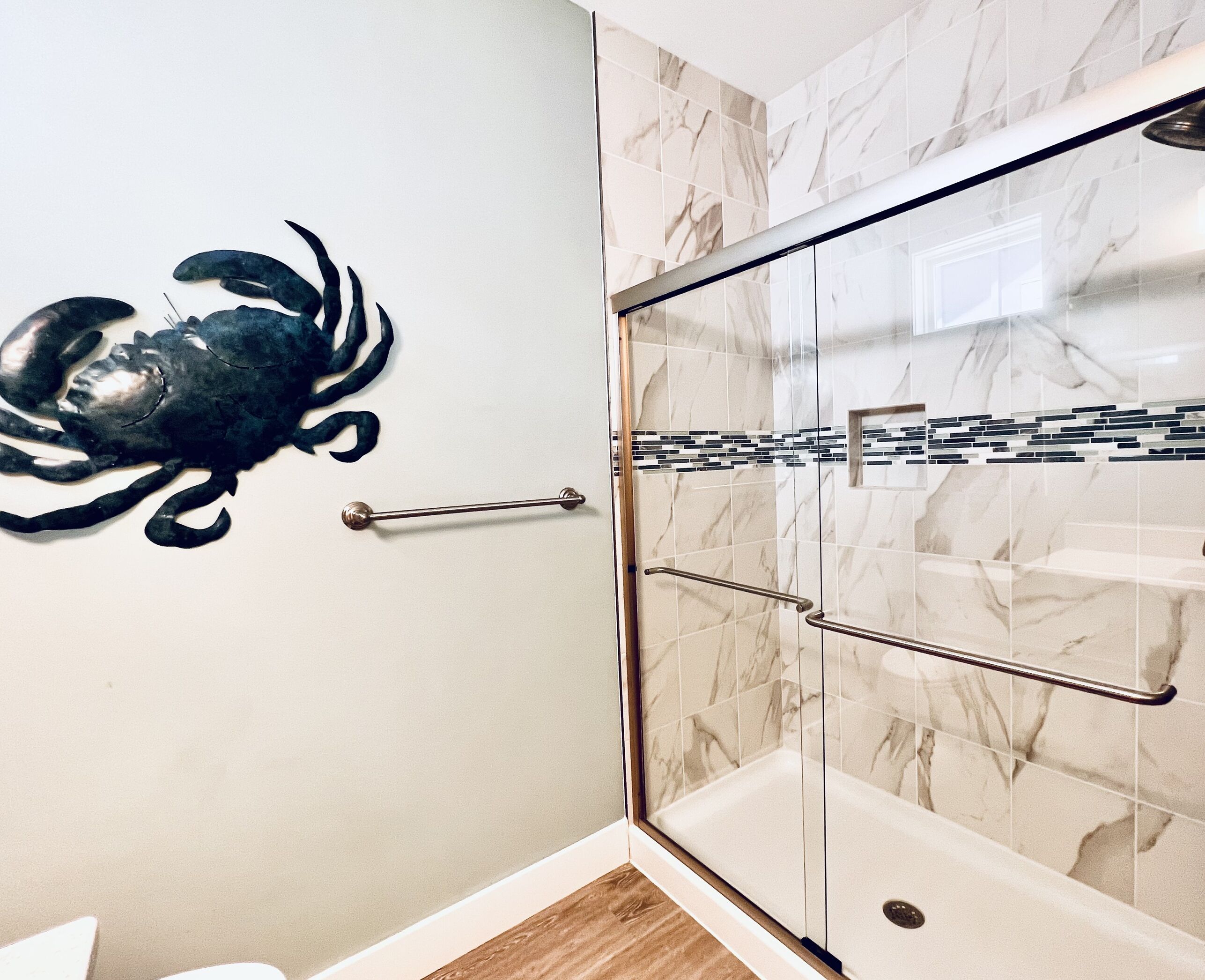 Une douche avec des portes en verre, un pare-baignoire en marbre et une barre d’appui en métal.