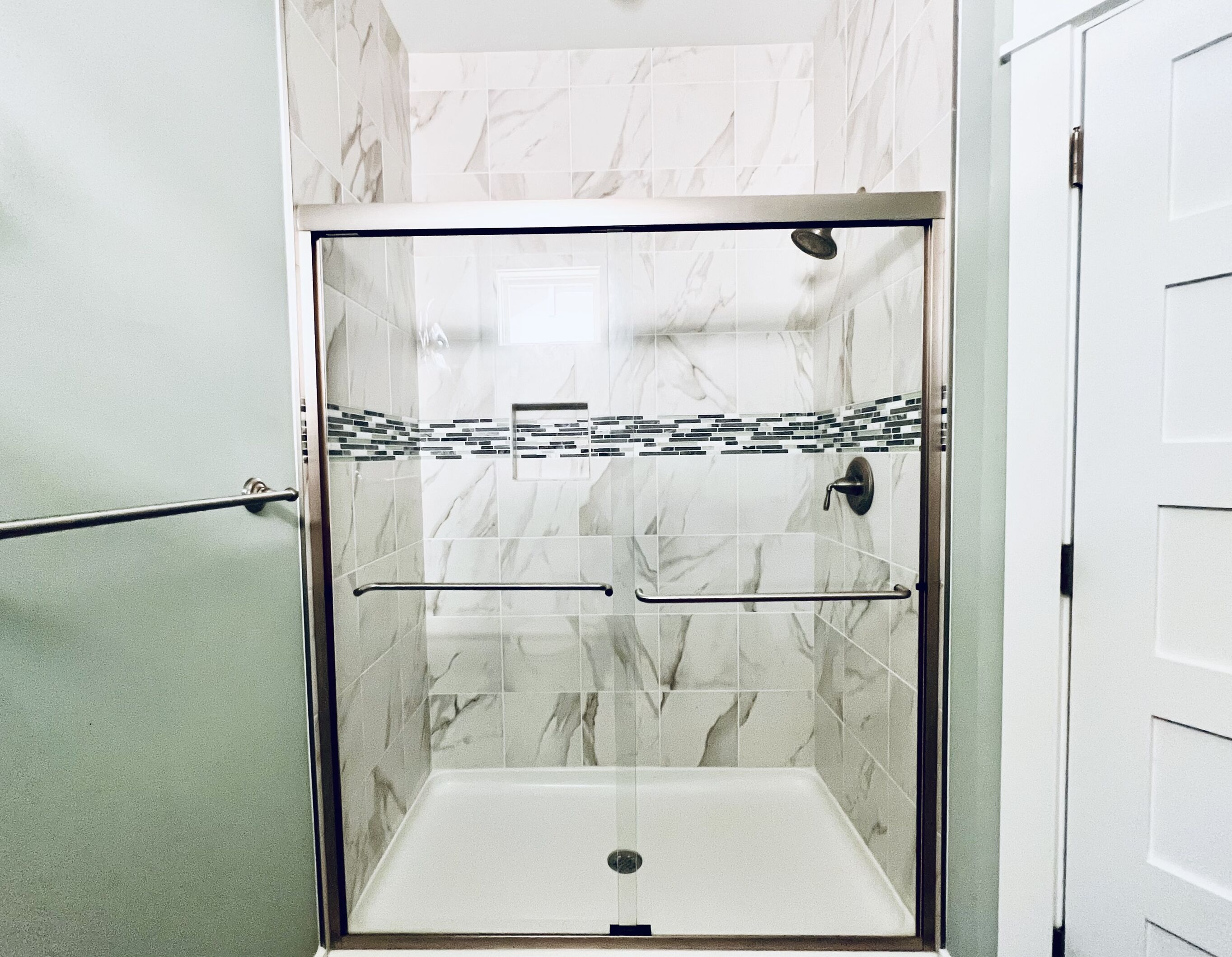 Eine gläserne Dusche mit Marmorwand, einem Metallgriff und einem gefliesten Boden.