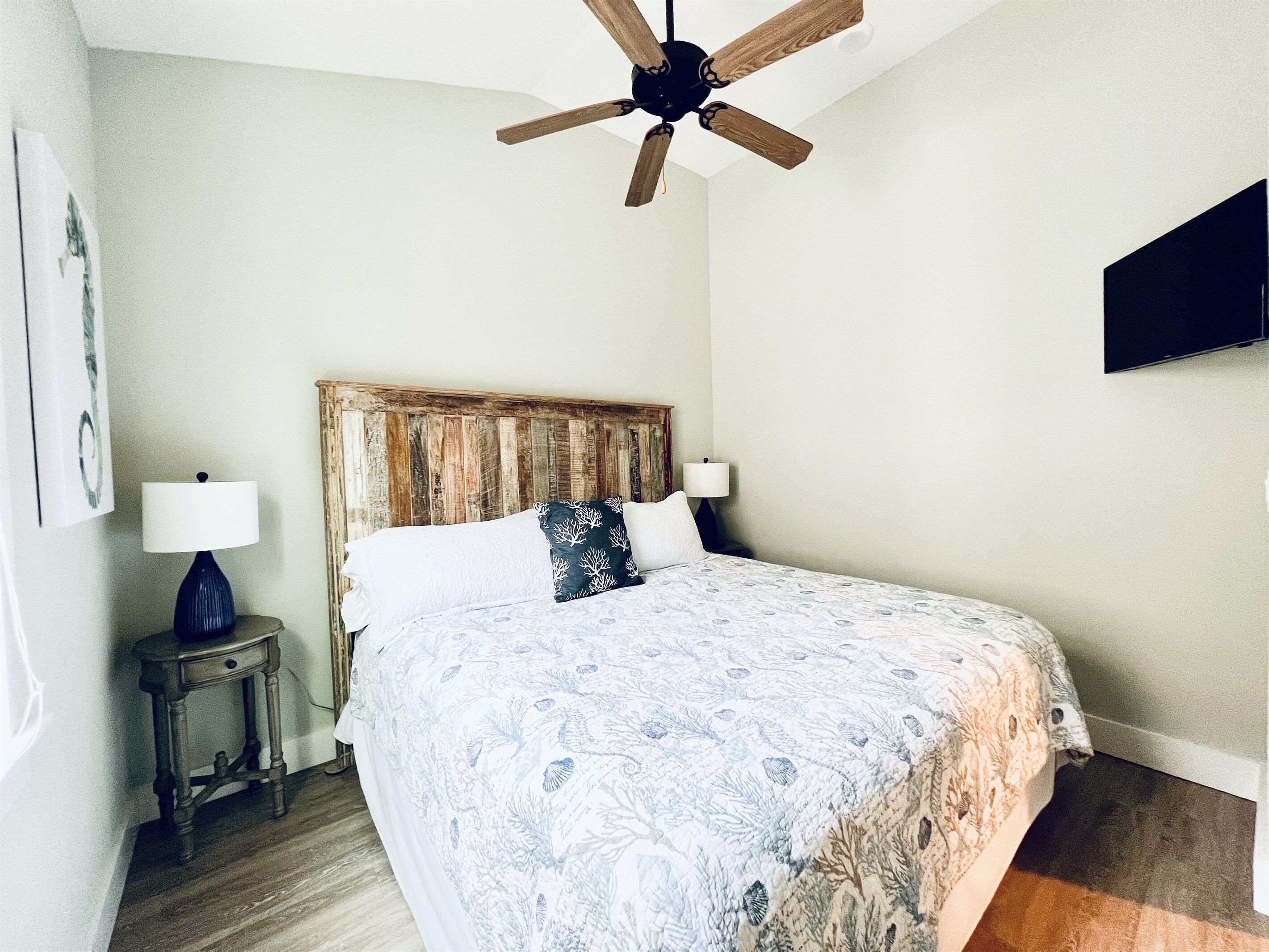 A bedroom with a wooden headboard, a bed with patterned bedding, a nightstand with a lamp, and a ceiling fan.