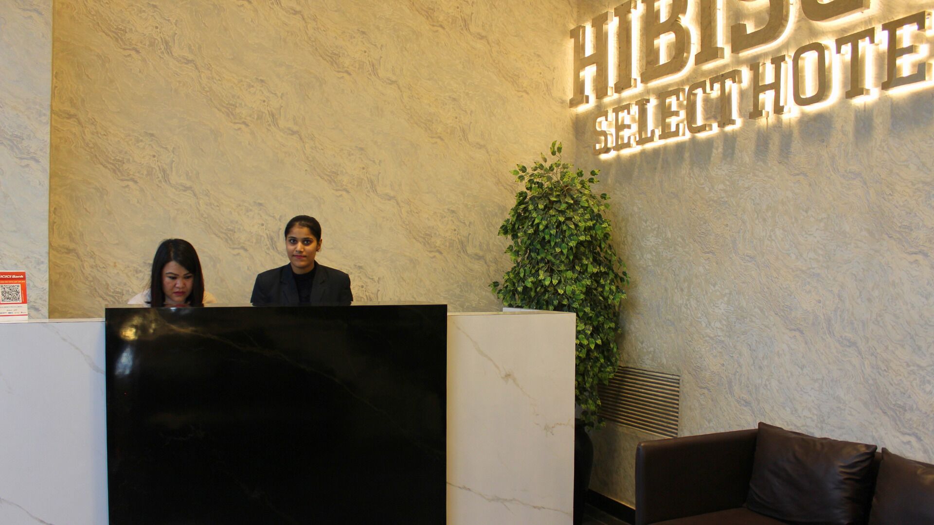 A reception desk with a marble top, a large potted plant, and a sign reading "HIBID HOTEL SELECT".