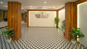 Un área de recepción con piso de diseño geométrico, paneles de madera y un cartel que dice 'Hibiscus Select Hotels'.