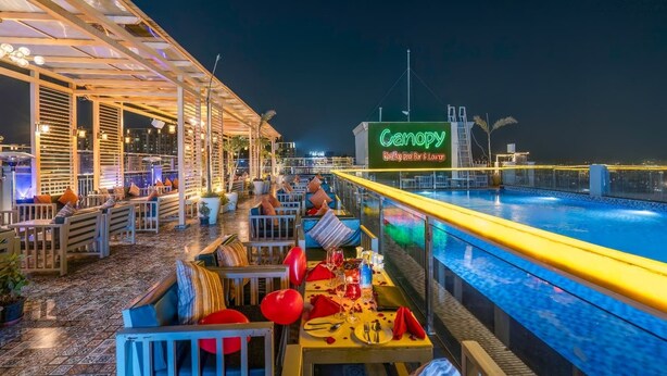 Un bar en la azotea con asientos al aire libre y una piscina, con un letrero de neón que dice 'Canopy Rooftop Bar & Lounge'.