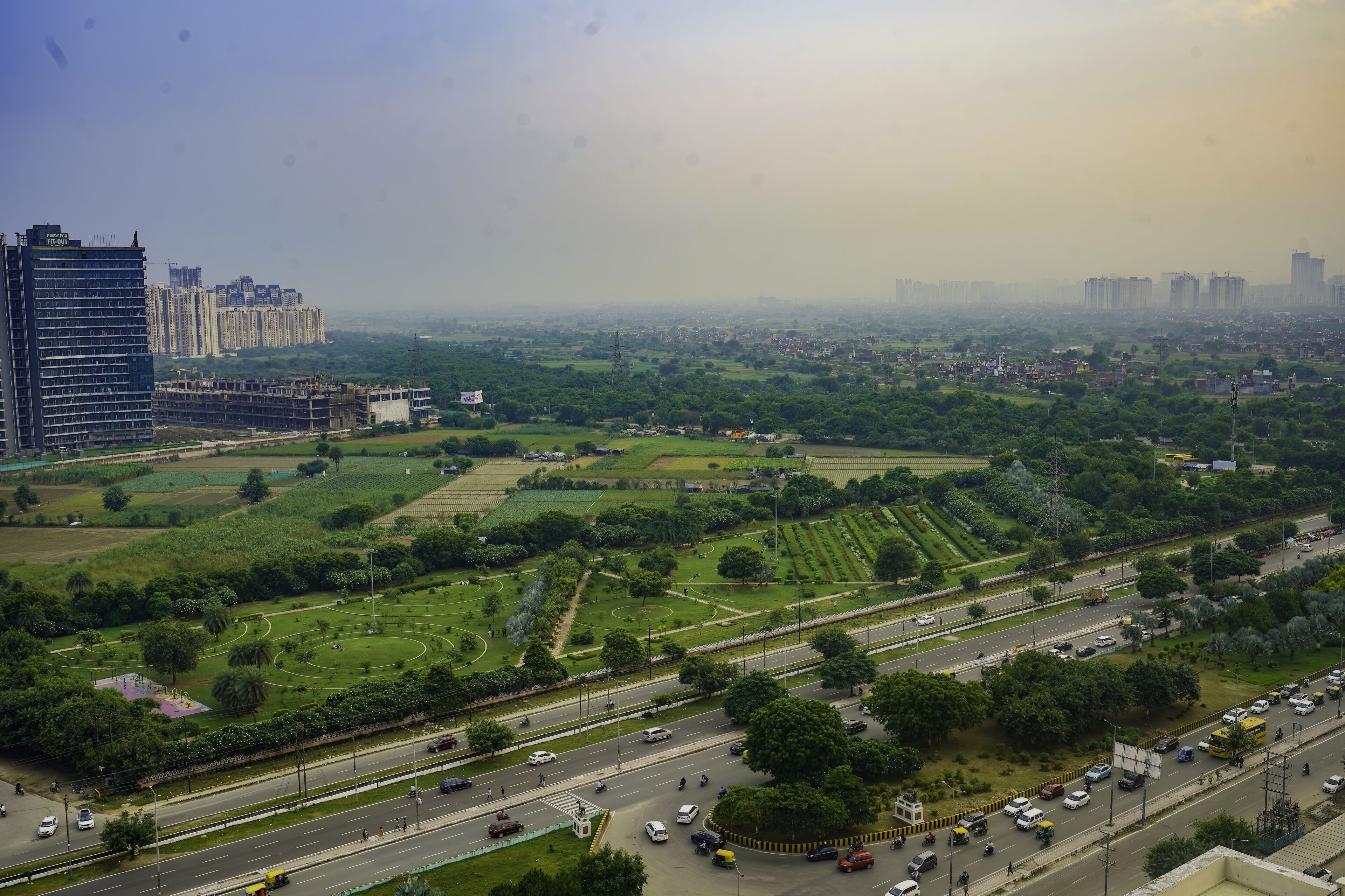 Un paysage urbain mêlant immeubles de grande hauteur et espaces verts, notamment un grand parc doté de sentiers et d’une aire de jeux.