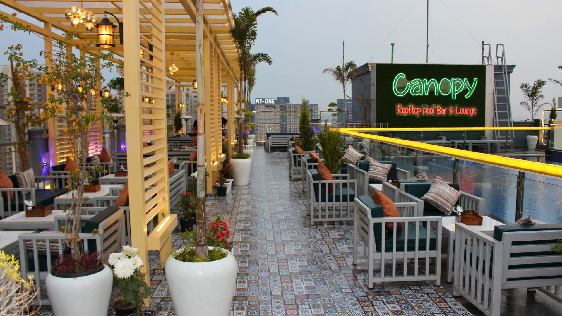 Een dakterras met terras, plantenbakken en een neonbord voor 'Canopy Rooftop Pub & Lounge'.