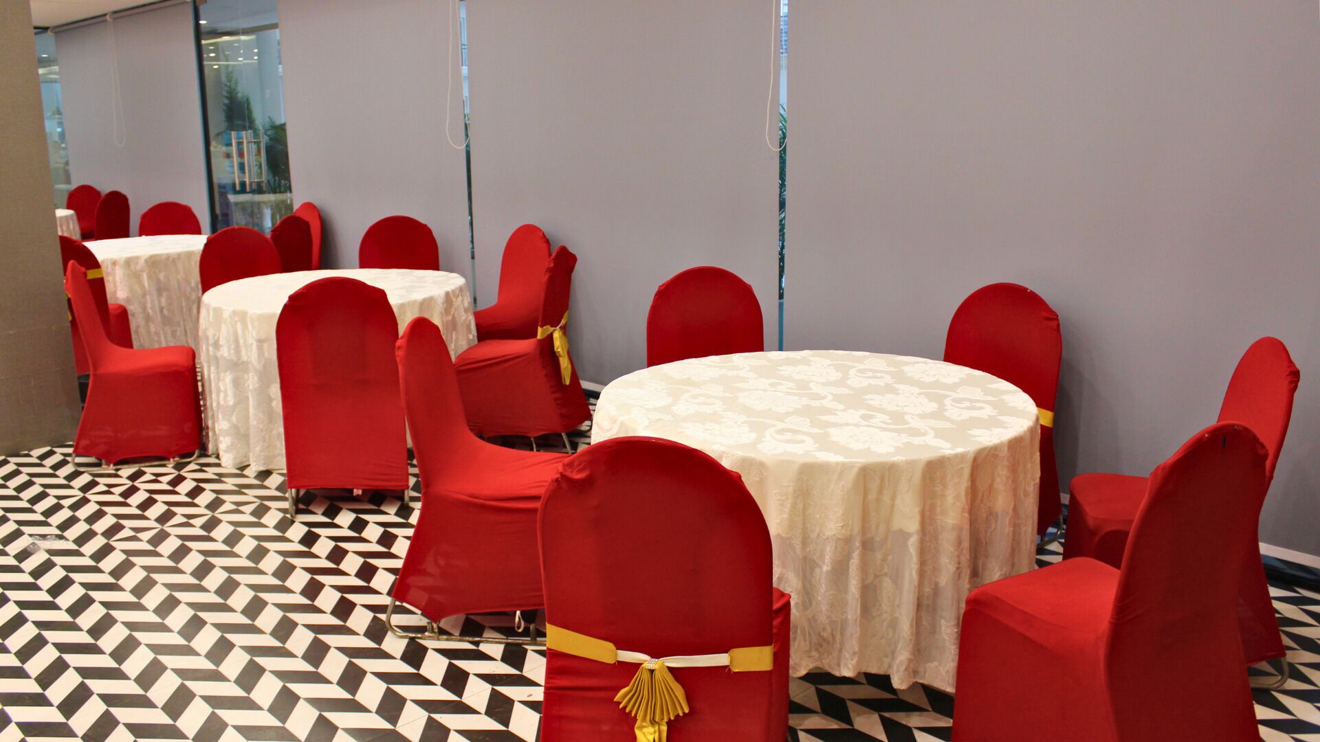 Un salón de conferencias con mesas redondas y sillas rojas, un suelo con diseño y una pared lisa.