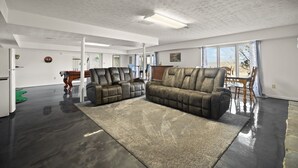 A spacious living room with a large sectional sofa, a dining area with a wooden table and chairs, and a view of the outdoors through large windows.