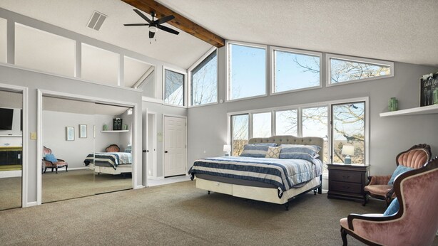 A spacious bedroom with a large bed, a chair, and a desk. There are multiple windows providing natural light and a view of the outdoors.