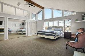 Un dormitorio amplio con una cama grande, una silla y un escritorio. Varias ventanas ofrecen luz natural y vistas al exterior.