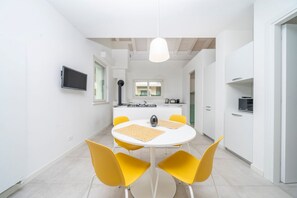 Een moderne keuken met witte kasten, een centraal eiland en een eethoek met een ronde tafel en gele stoelen.
