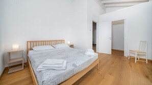 A bedroom with a wooden bed, white walls, a nightstand, a chair, and a door leading to another room. - La Casa di Antonietta (Udine)