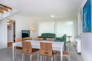 A modern living room with a dining area, a green sofa, and a flat-screen TV.