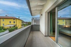 Een balkon met uitzicht op omliggende gebouwen, een glazen deur en een betegelde vloer.