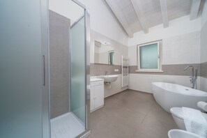 Een moderne badkamer met een douchecabine van glas, een vrijstaand bad, een wastafel en een spiegel.